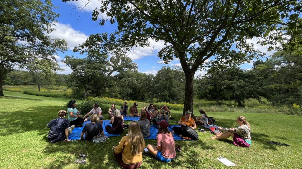 therapists attending a retreat session on tarps outside under an oak tree