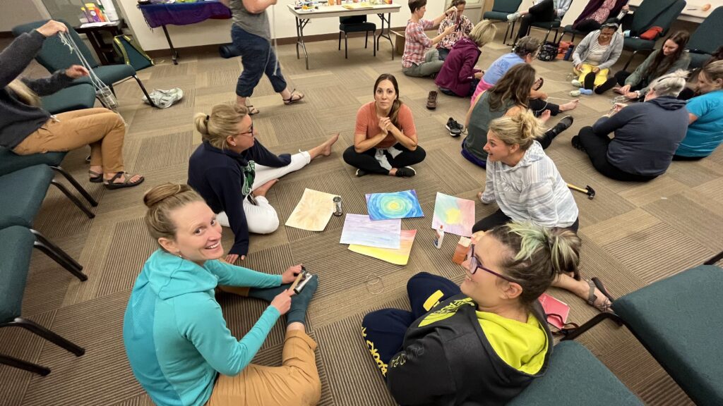 Two small groups of therapists sitting on the floor working on a craft and having discussion at the nature based therapy retreat